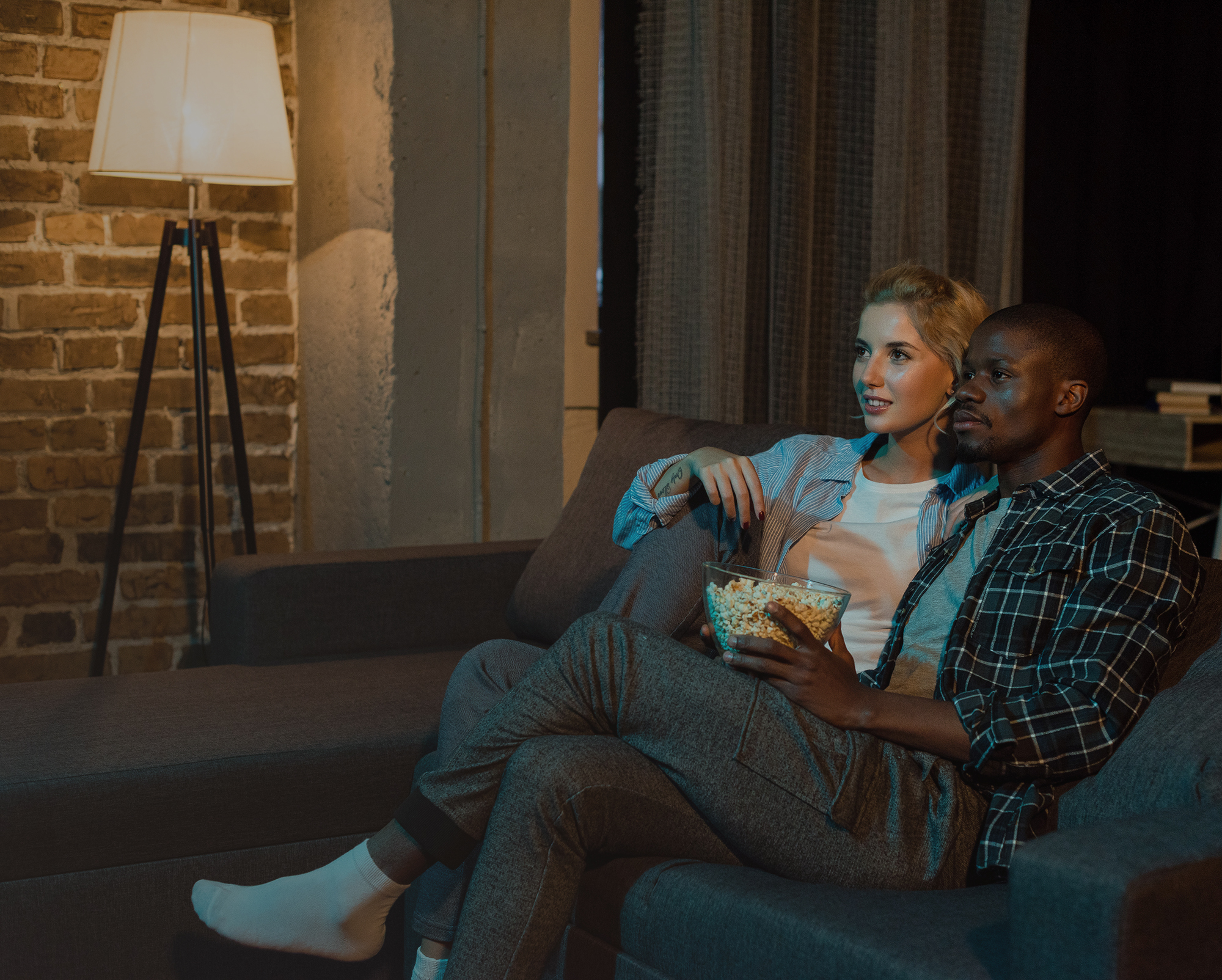 young multiethnic couple with popcorn watching film together on sofa at home